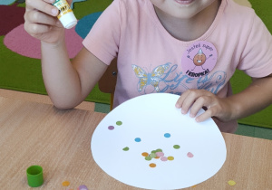 Dziewczynka siedzi przy stoliku i wykonuje pracę plastyczną