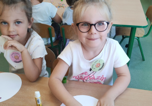Dziewczynki siedzą przy stoliku i wykonują pracę plastyczną