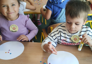 Dzieci siedzą przy stoliku i wykonują pracę plastyczną
