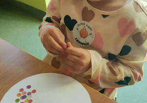 Dziewczynka siedzi przy stoliku i wykonuje pracę plastyczną