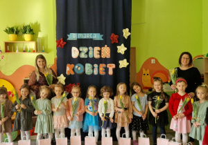 Dziewczynki wraz z Paniami pozują do zdjęcia na tle dekoracji "Dzień Kobiet"