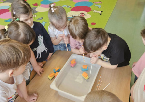 Dzieci dmuchają przez słomkę na statki, które znajdują się w pojemniku z wodą.