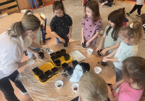 Druga grupa dzieci uzupełnia doniczki ziemią i nasionami rzeżuchy.