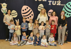 Dzieci z paniami stoją na tle dekoracji.