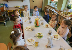 Dzieci siedzą przy stole i spożywają posiłek.