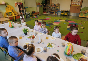 Dzieci siedzą przy stole i jedzą śniadanie.