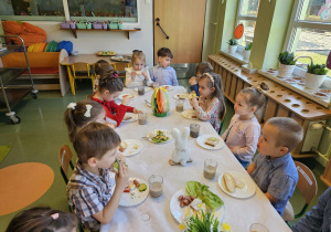 Dzieci siedzą przy stole i jedzą śniadanie.