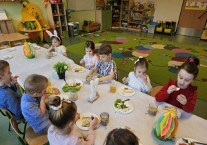 Dzieci siedzą i spożywają wielkanocne śniadanie.