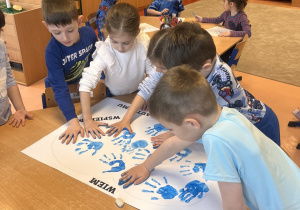 Chłopcy i dziewczynki odbijają niebieską dłoń na papierze.