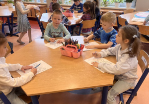 Przedszkolaki kolorują motyla i wycinają go przy stolikach.