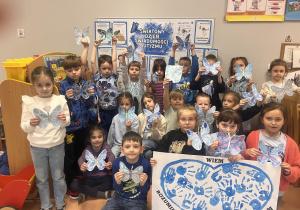 Zdjęcie grupowe z pracami platycznymi na tle dekoracji.