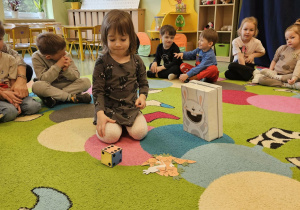 Dziecko siedząc na dywanie rzuca kostką.