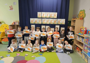 Dzieci stoją na tle materiału z pracą plastyczną.