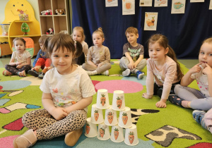 Dziewczynka siedzi obok ułożonych kubeczków.