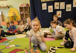 Dziecko siedzi na tle materiału przy posadzonych marchewkach.