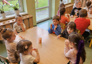 Dzieci siedzą przy stoliku i jedzą marchewkę.
