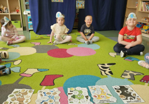 Dzieci siedzą na tle granatowego materiału, a w środku leżą kosze z posegregowanymi śmieciami.