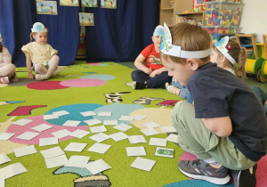 Dzieci siedzą na dywanie i grają w memory.