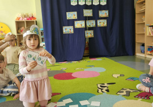 Dziewczynka siedzi na dywanie i pokazuje parę obrazków.