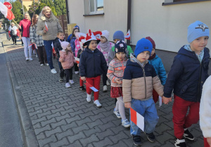 Przedszkolaki z flagami idą przed domem.