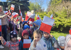 Przedszkolaki stoją z flagami uniesionymi w górę.