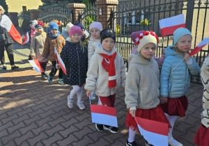 Przedszkolaki z flagami idą przez miasto.