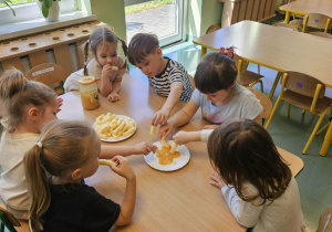 Dzieci siedzą przy stoliku i jedzą miód.