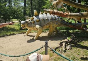 Na fotografii widać dużego dinozaura i małego siedzącego na gałęzi.