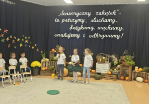 Chłopiec i dziewczynki stoją na tle dekoracji i mówią wiersz.