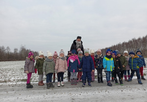 Dzieci z nauczycielką w zimowym krajobrazie.