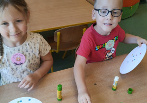 Dzieci siedzą przy stoliku i wykonują pracę plastyczną