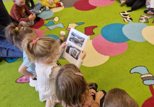 Dzieci siedzą w kole i oglądają zdjęcia skarbonek