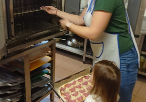 pani kucharka z dziewczynką wkłada pizzę do piekarnika