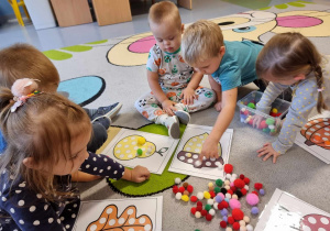 Dzieci siedzą na dywanie i układają kolorowe pompony na obrazkach