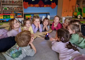 Dzieci leżąc na dywanie patrzą na kulę świetlną