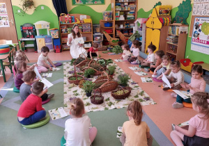 Dzieci siedzą w kole na dywanie podczas warsztatów zielarskich