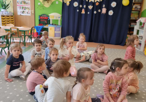 Dzieci siedzą na dywanie na tle dekoracji