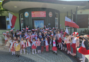 Dzieci pozują do wspólnego zdjęcia z flagami Polski na tle budynku przedszkola