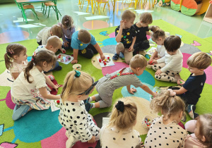 Dzieci na dywanie układają kolorowe pompony na kartach pracy