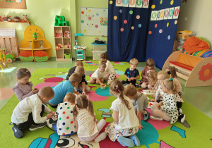 Dzieci na dywanie układają kolorowe pompony na kartach pracy