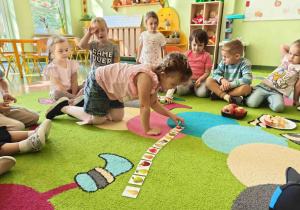 Dzieci siedzą na dywanie podczas zajęć dydaktycznych i wykonują ćwiczenia