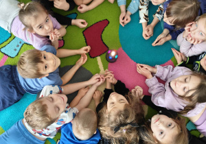 Dzieci leżą na dywanie i przyglądają się świecącej kuli