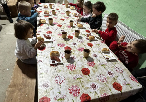 Dzieci siedzą przy stole i jedzą kiełbaskę