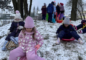 Dzieci zjeżdżaja na sankach z górki.