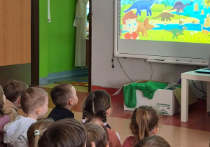 dzieci oglądają film edukacyjny o dinozaurach